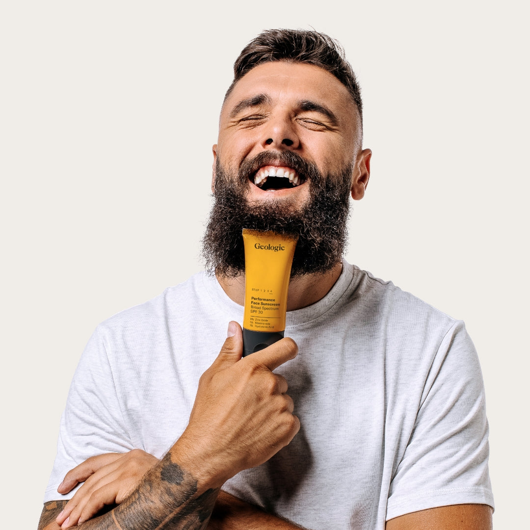 Bearded man holding Geologie's Anti Aging Duo and laughing.