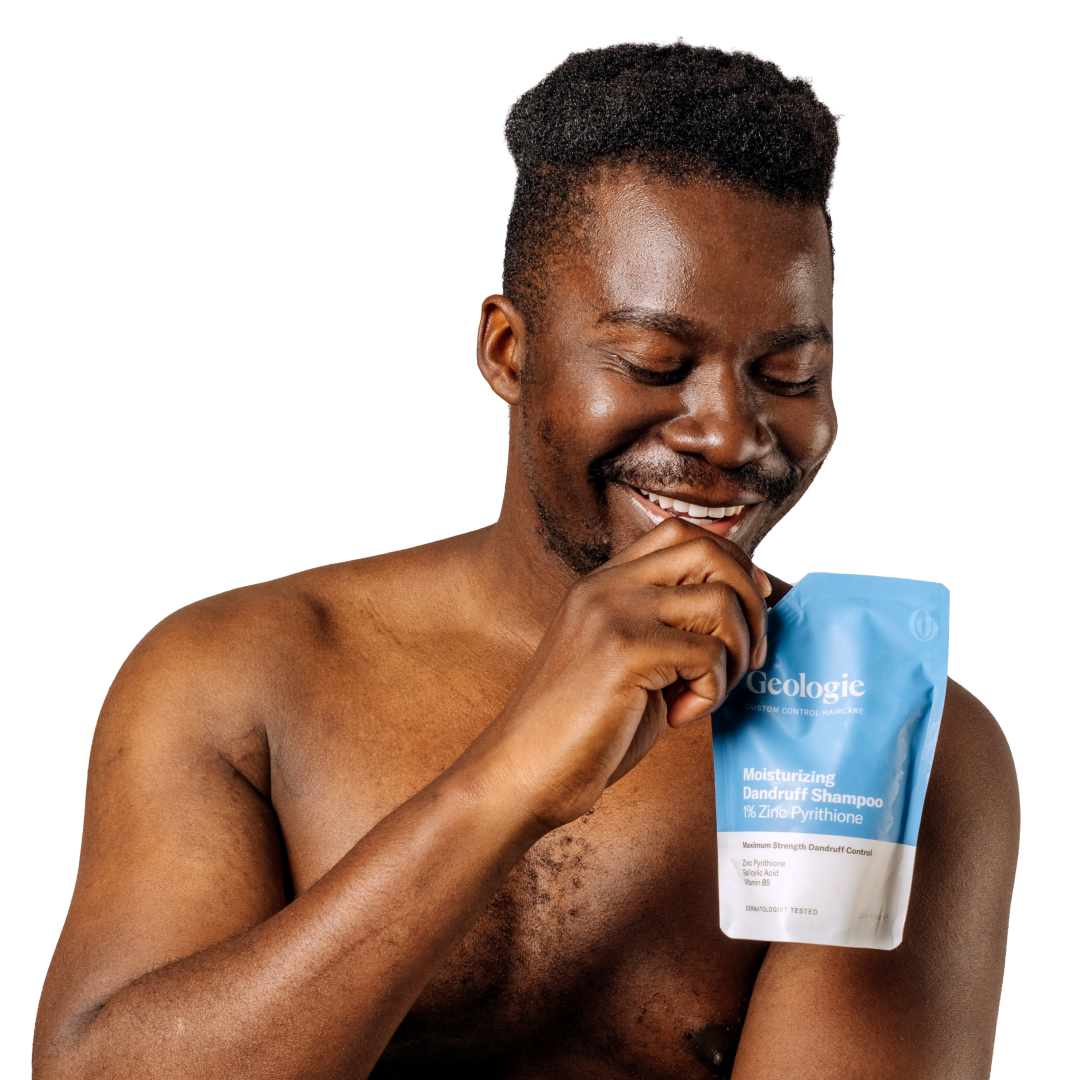 A cheerful man holding a bag of Geologie's Dandruff Shampoo + Conditioner Bundle that prevents dandruff.