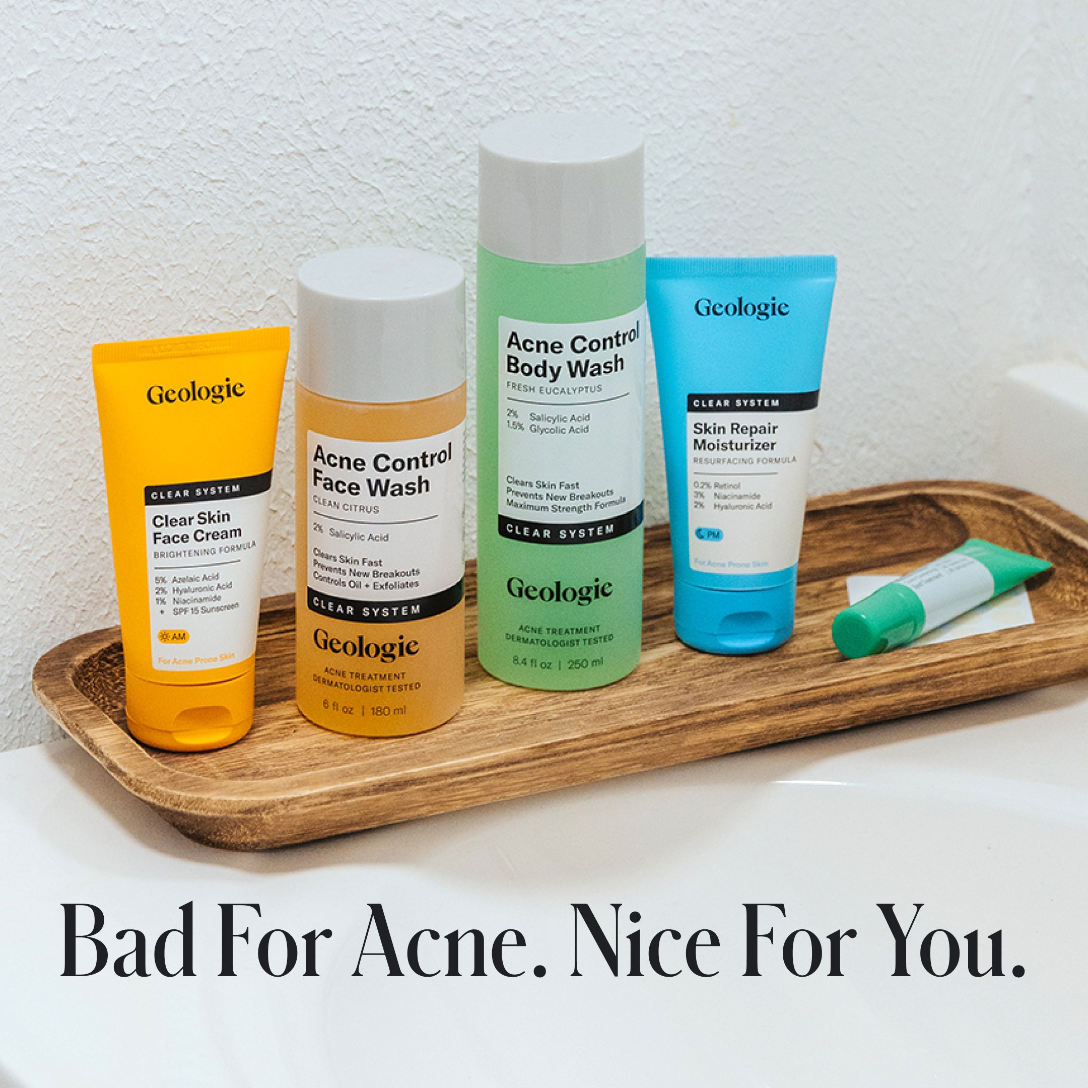 Four Geologie Clear Skin Face Cream products, featuring azelaic acid, are displayed on a wooden tray with the tagline Bad For Acne. Nice For You.—showcasing their Clear Skin Face Cream Acne Treatment System.