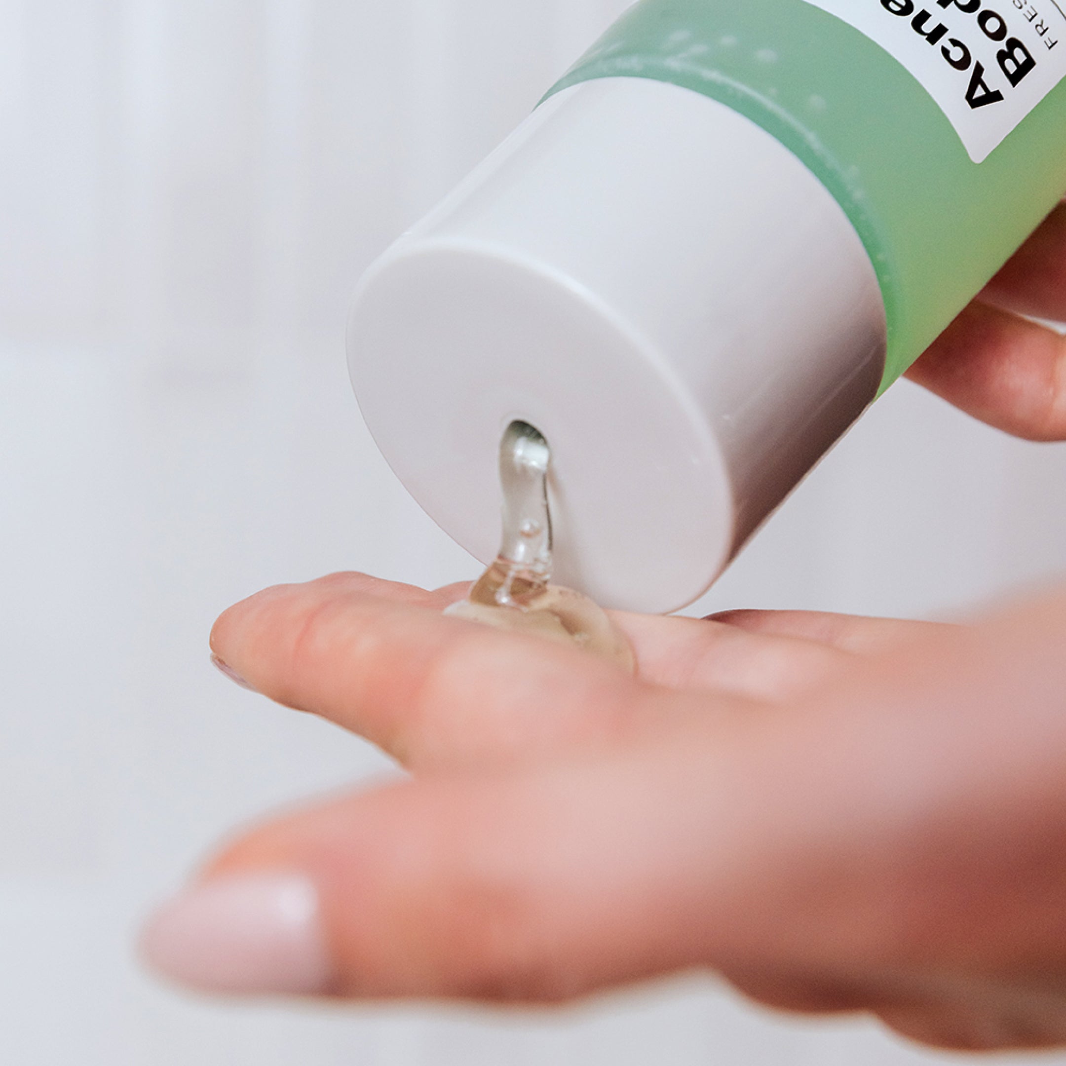 A close-up of a person dispensing Geologie Acne Control Body Wash with Salicylic Acid from a green and white bottle onto their hand.